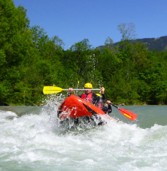 Spritzende Wellen beim Rafting Klassiker auf der Iller. Das Canadier Boot reitet durch die weiße Gischt.